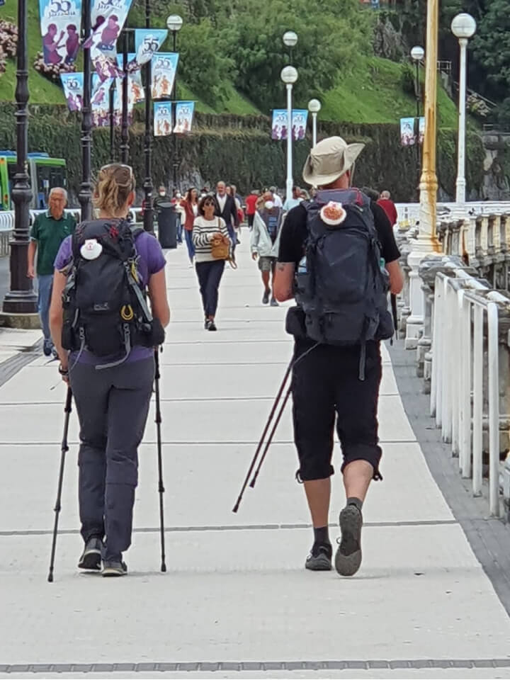 photo of two pilgrims with packs and hiking sticks walking on the promenade in San Sebastian