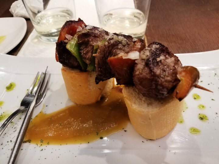 photo of a pincho of beef kabab arranged over two slices of bread with an apple reduction from San Sebastian